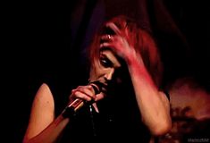 a woman with red hair holding a microphone in front of her face and singing into the microphone