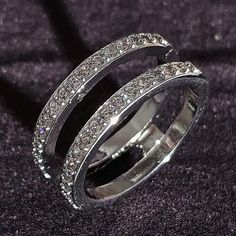 two silver rings with diamonds on them sitting on a black clothed surface in front of a dark background