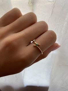 a woman's hand wearing a gold ring with an emerald stone in the middle