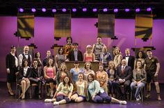 a group of people sitting on top of a stage next to each other in front of purple walls