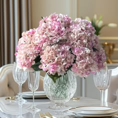 a vase filled with pink flowers sitting on top of a dining room table next to two wine glasses