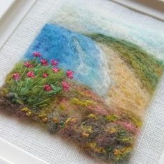 there are flowers in the grass on this piece of art that is made out of wool