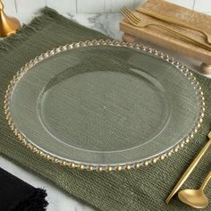 a place setting with silverware and green napkins on a marble countertop next to gold - plated utensils