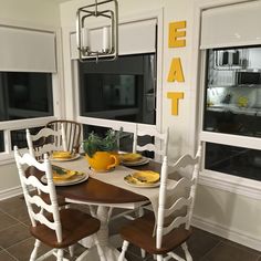 a dining room table with chairs and plates on it in front of two windows that have the word eat painted on them