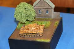 a small toy tank sitting on top of a wooden box next to a tree and house