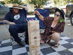 a man and woman sitting in lawn chairs next to a giant wooden block tower on a checkered floor