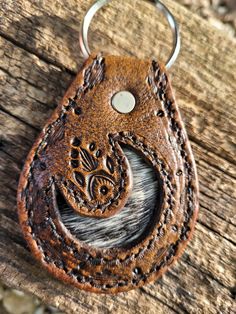 a leather keychain with an intricate design on the front and back ends, hanging from a wooden surface