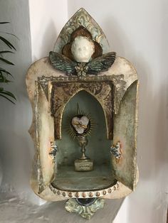 an ornate clock is on the wall next to a potted plant in a corner