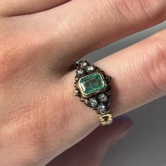 a woman's hand with a green ring on top of her finger and diamond accents around the band