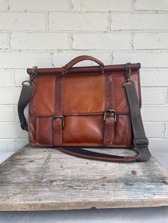 This is a great brown leather satchel. It is a great size to fit most laptops. The front has two buckle straps that have click in brass attachments. There are plenty of pockets inside and out to hold a number of needed cords, pens etc.. This bag has the most wonderful patina to it. It will expand but is about 5" deep without anything in the bag. It has an adjustable strap to wear it as a crossbody. Perfect for a man or woman. The inside is very clean. 16"x12"x5" Brown Saddle Bag With Adjustable Strap For Office, Brown Office Saddle Bag With Adjustable Strap, Classic Brown Laptop Bag For Travel, Brown Flap Satchel With Adjustable Strap, Classic Leather Shoulder Bag With Buckle Closure, Brown Satchel Briefcase For Travel, Classic Leather Bags With Buckle Closure, Classic Leather Bag With Buckle Closure, Classic Brown Saddle Bag With Adjustable Strap