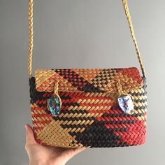 a hand holding a woven purse with blue stones on the front and red, black, yellow, and orange stripes