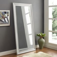 a white floor mirror sitting on top of a wooden floor next to a vase filled with flowers