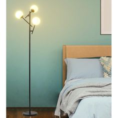 a floor lamp with three lights on it next to a bed