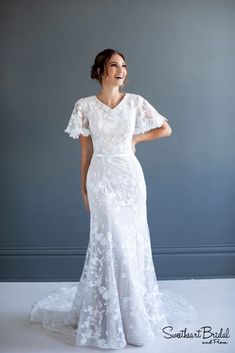 a woman in a white wedding dress standing with her hands on her hips and smiling