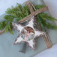 a star ornament with an angel on it next to twigs and greenery