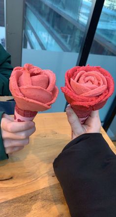 two hands holding pink flowers on top of a wooden table