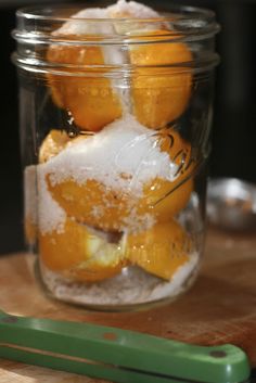 some oranges are sitting in a glass jar on a table next to a spoon