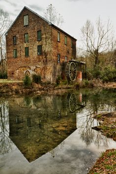 an old brick building sitting next to a body of water with trees in the background