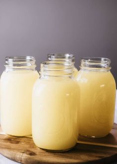 three jars filled with yellow liquid sitting on top of a wooden cutting board