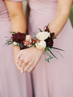 two bridesmaids in pink dresses hold their bouquets with flowers on the wrist