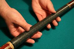 a pool cue being held by someone's hand on a green cloth covered pool table