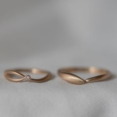 two gold wedding rings sitting on top of a white cloth covered tablecloth, one with a diamond in the middle