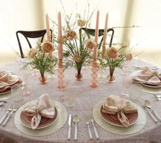 a table set with plates, silverware and pink flowers in vases on it