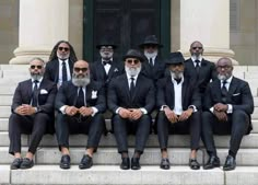 a group of men in suits and hats sitting on steps with one man wearing sunglasses