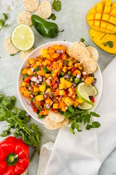 a white bowl filled with mango salsa next to tortilla chips and lime wedges