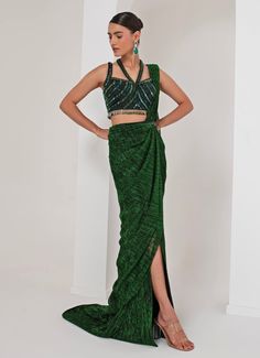 This elegant Emerald Green Pre-Draped Saree is meticulously crafted from a luxurious blend of crepe and platinoir crepe, offering a rich texture and impeccable drape. The green saree merges traditional charm with modern flair, featuring all-over metallic detailing that adds a subtle, luxurious sheen. Paired with a sleeveless halter neck blouse, intricately adorned with dangling halo nalki embellishments, making it both chic and sophisticated. A hand-embellished belt cinches the waist, adding a contemporary edge to this timeless look. Perfect for cocktails, Sangeet nights, or evening parties, this outfit ensures you stand out with grace, elegance, and style. Composition : Blouse - Crepe blend, Saree - Platinoir Crepe Care: Dry Clean Only and Vacuum Storage This product can be customized for Green Silk Pre-draped Saree, Green Georgette Draped Saree, Green Pre-draped Saree For Reception, Green Blouse Piece For Evening With Traditional Drape, Green Draped Lehenga With Cutdana, Green Draped Saree With Unstitched Blouse, Elegant Draped Green Lehenga, Formal Pre-draped Saree With Zari Work, Green Silk Pre-draped Saree For Evening