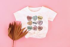 a baby t - shirt with hearts on it next to a palm leaf and pink background