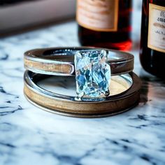 a diamond ring sitting on top of a marble table next to two bottles of wine