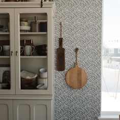 a kitchen with wall paper and wooden utensils hanging on the wall next to a china cabinet