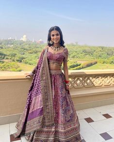 a woman in a purple and pink lehenga standing on a balcony overlooking the city