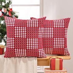 two red and white pillows sitting on top of a wooden bench next to a christmas tree