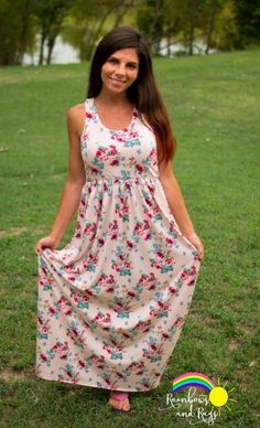 a woman standing in the grass wearing a dress with flowers on it and smiling at the camera