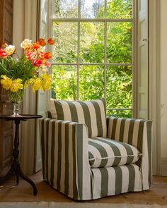 a striped chair sitting in front of a window next to a vase with flowers on it