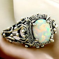 Introducing a stunning piece of history and craftsmanship: our Vintage Estate Lab Created Cabochon Opal Solitaire Filigree Ring. This exquisite ring is meticulously crafted from solid 925 sterling silver, showcasing the timeless beauty of filigree work that adds intricate elegance to any outfit. The centerpiece of this enchanting ring is a high-quality lab created opal stone, measuring 8x6 mm, which radiates hues of mesmerizing blue and green, mirroring the shimmering depths of the ocean. With the top of the ring measuring nearly 1/2 inch in length, it's a standout piece that draws admiration without being overwhelming. Not only does this ring embody vintage glamour, but it also represents a commitment to sustainability. This stunning ring is stamped with "925," ensuring you receive authen Classic Wedding Jewelry With Cabochon, Vintage Hallmarked Opal Ring For Anniversary, Silver Opal Ring With Stone Setting For Anniversary, Vintage Opal Birthstone Ring Gift, Classic Gift Opal Ring, Heirloom Jewelry With Intricate Design For Collectors, White Victorian Jewelry For Ceremonial Occasion, Classic Sterling Silver Opal Birthstone Ring, Antique Sterling Silver Jewelry With Birthstone