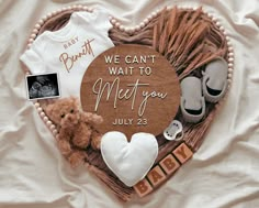 a heart shaped sign with baby clothes and teddy bears on it that says, we can't wait to meet you july 25