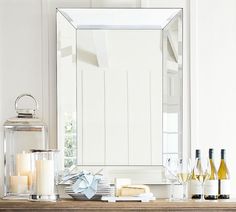 a table topped with candles and bottles of wine next to a large mirror on top of a wooden shelf