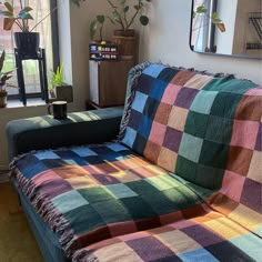 a couch covered in a multicolored checkered blanket sitting next to a window