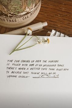 a piece of paper sitting on top of a table next to a pen and flower