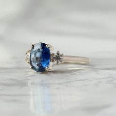 With a brilliant cut like that, this ring is nothing but pure brilliance in itself. With a lovely Kyanite, the Khloe ring with two side moissanite sparkles like there is no tomorrow. Celebrate your milestones or special occasions with this ring as the perfect gift for sisters as a best friend's gift, or just as an everyday celebration of life in general. Details: Center stone Gemstone: Kyanite Stone Shape: Oval Measurements: approx. 9x7mm Side stones Gemstone: Moissanite Shape: Round Measurement Oval Brilliant Cut Topaz Ring, Oval Halo Ring With Accent Stones For Promise, Promise Oval Halo Ring With Center Stone, Oval Halo Ring For Promise With Center Stone, Oval Crystal Promise Ring With Center Stone, Oval Crystal Ring With Center Stone For Promise, Oval Halo Ring For Promise - Fine Jewelry, Oval Diamond Promise Ring, Oval Halo Ring For Promise In Fine Jewelry Style