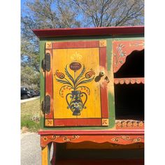 an old painted wooden cabinet in the middle of a parking lot with cars parked behind it