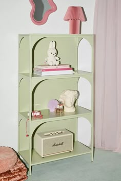 a green book shelf with pink lamps and other items on it in front of a mirror