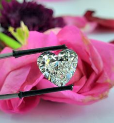 a heart shaped diamond sitting on top of two black pins in front of pink flowers