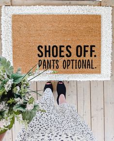 a person standing under a door mat that says shoes off pants optional