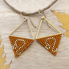 two pairs of triangle shaped earrings hanging from a string on a wooden table with leaves