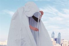 a woman dressed in white is holding her veil over her face