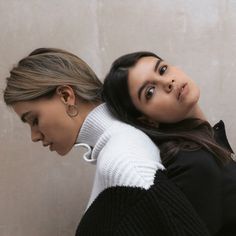 two women standing next to each other in front of a wall with their hair pulled back